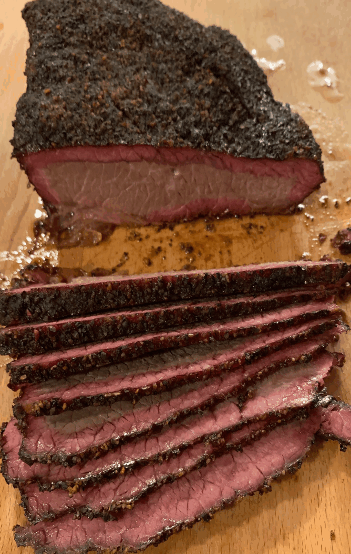 Sliced smoked brisket with a dark bark and juicy interior on a wooden board.
