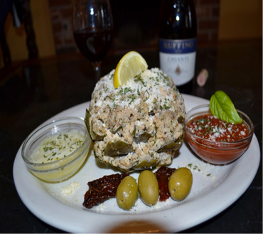 Plate with crab cake, sauces, olives, and lemon wedge.